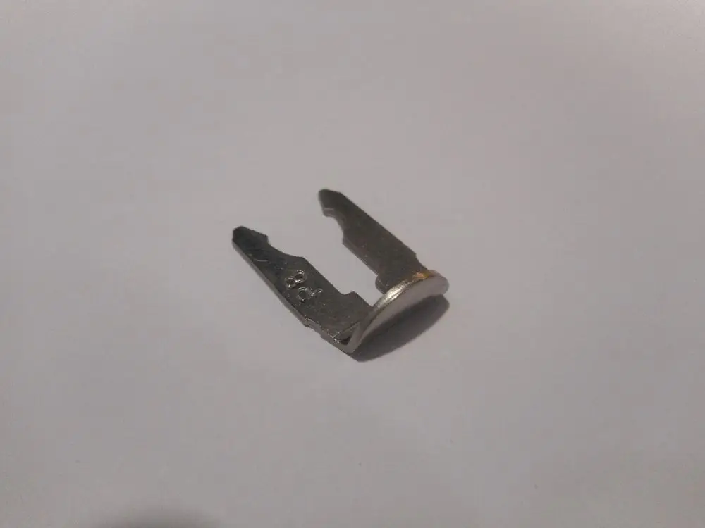 Remeha Clip, metallisch, mit einem flachen Ende und zwei Zinken, gekrümmt und asymmetrisch, auf weißem Hintergrund positioniert.